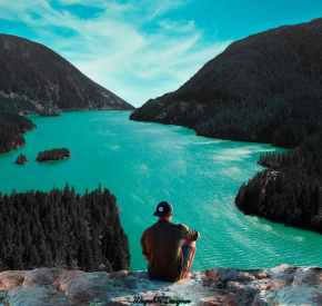 man sitting on cliff in front of body of water